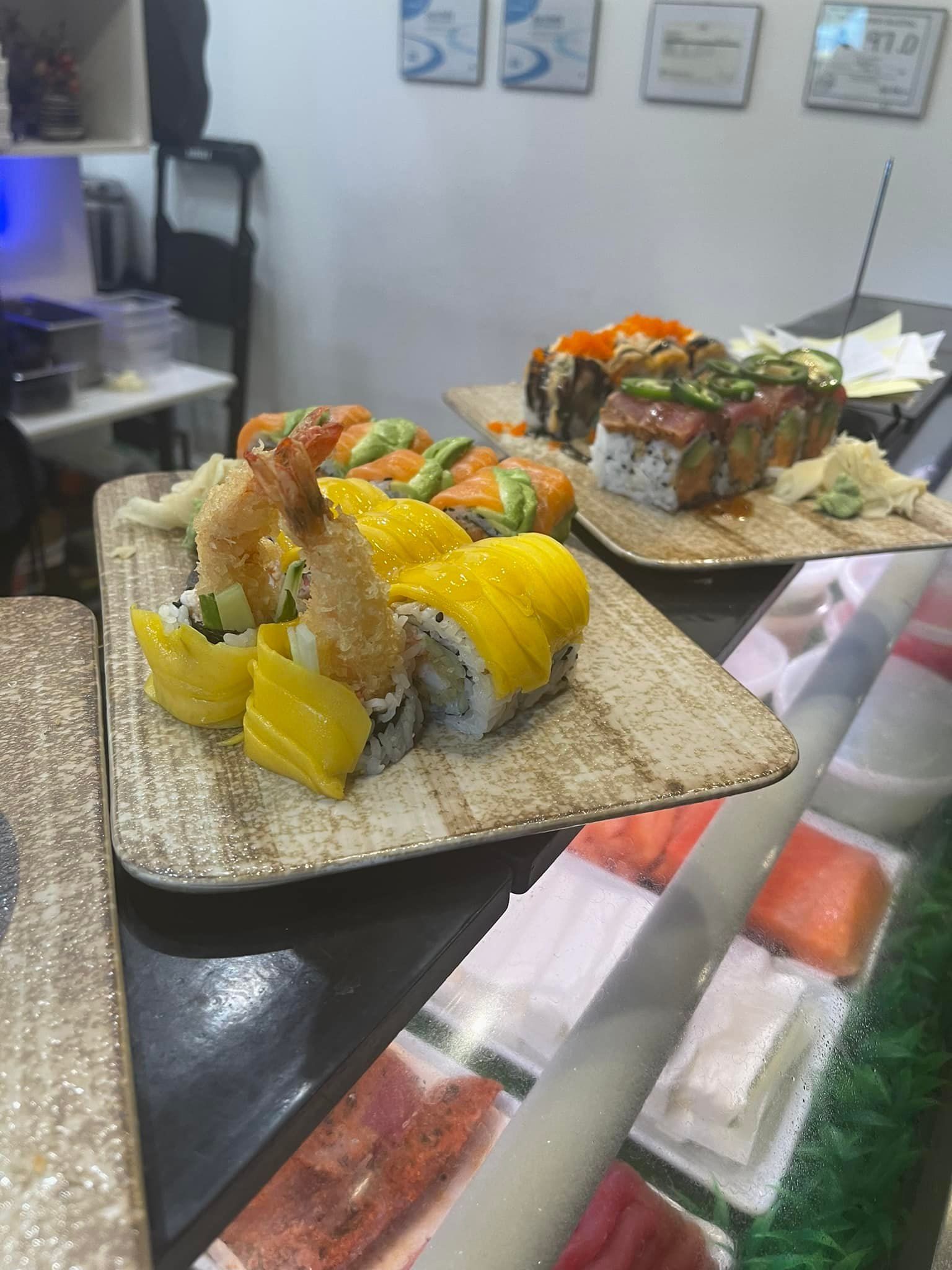 Sushi rolls on plates, variety of colors and toppings, displayed on a counter.
