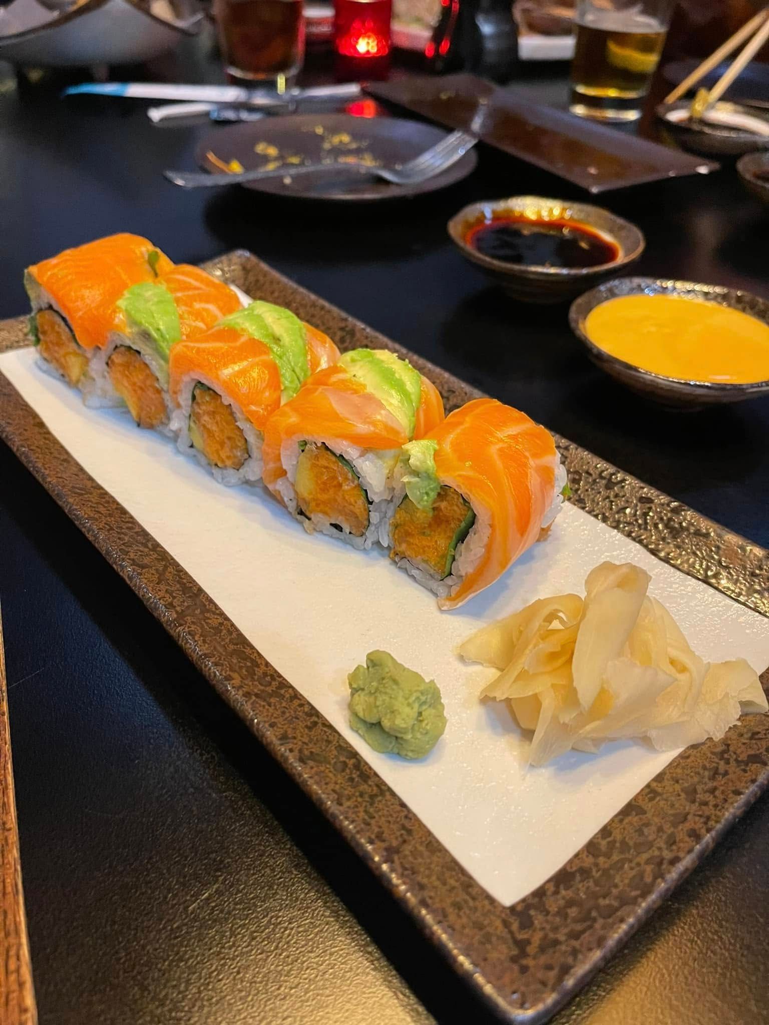 Sushi roll with salmon, avocado, and sauce on a rectangular plate, with wasabi and pickled ginger.