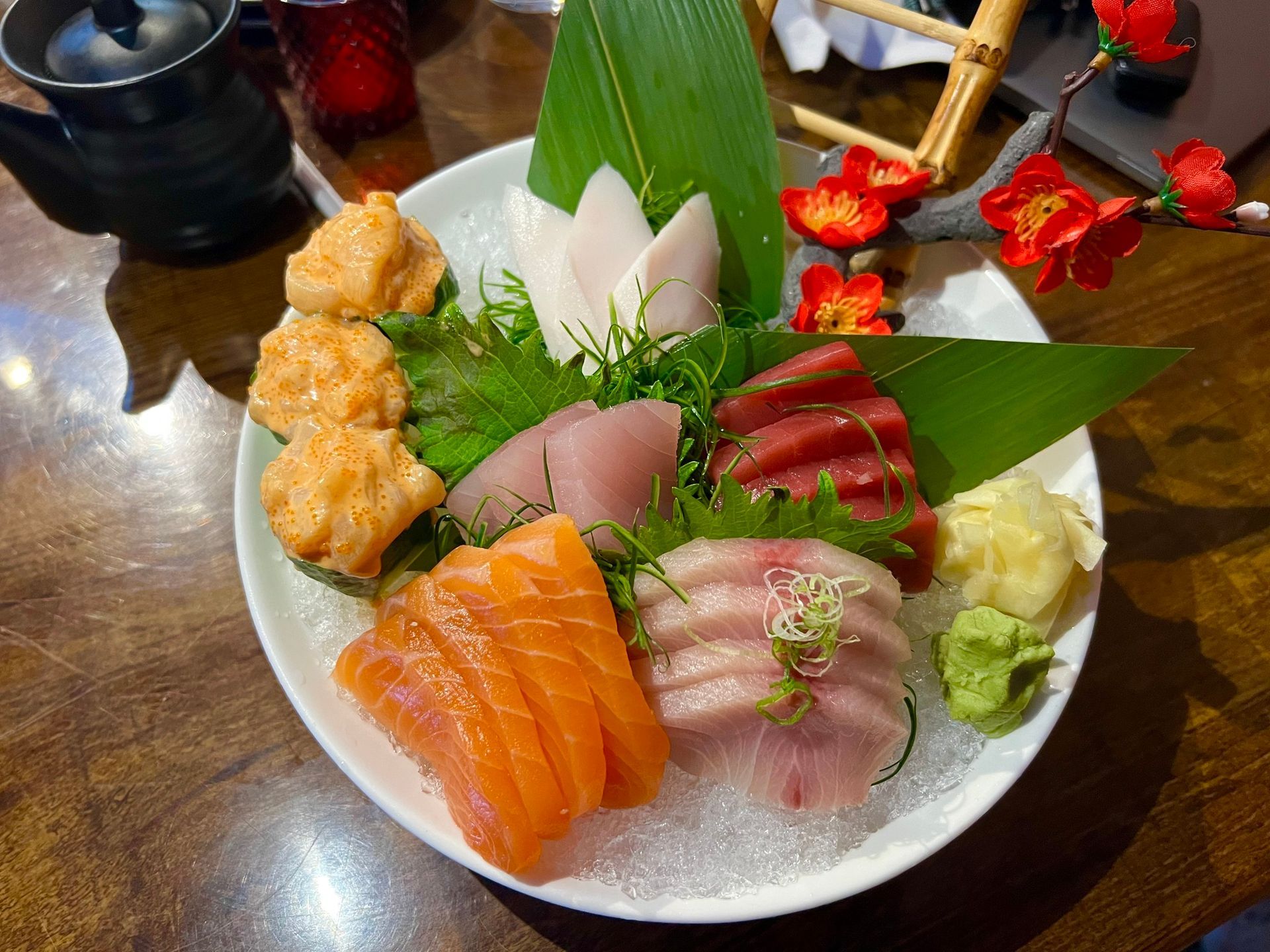 Sashimi platter with salmon, tuna, white fish, and fried tofu balls, garnished with wasabi and green leaves.