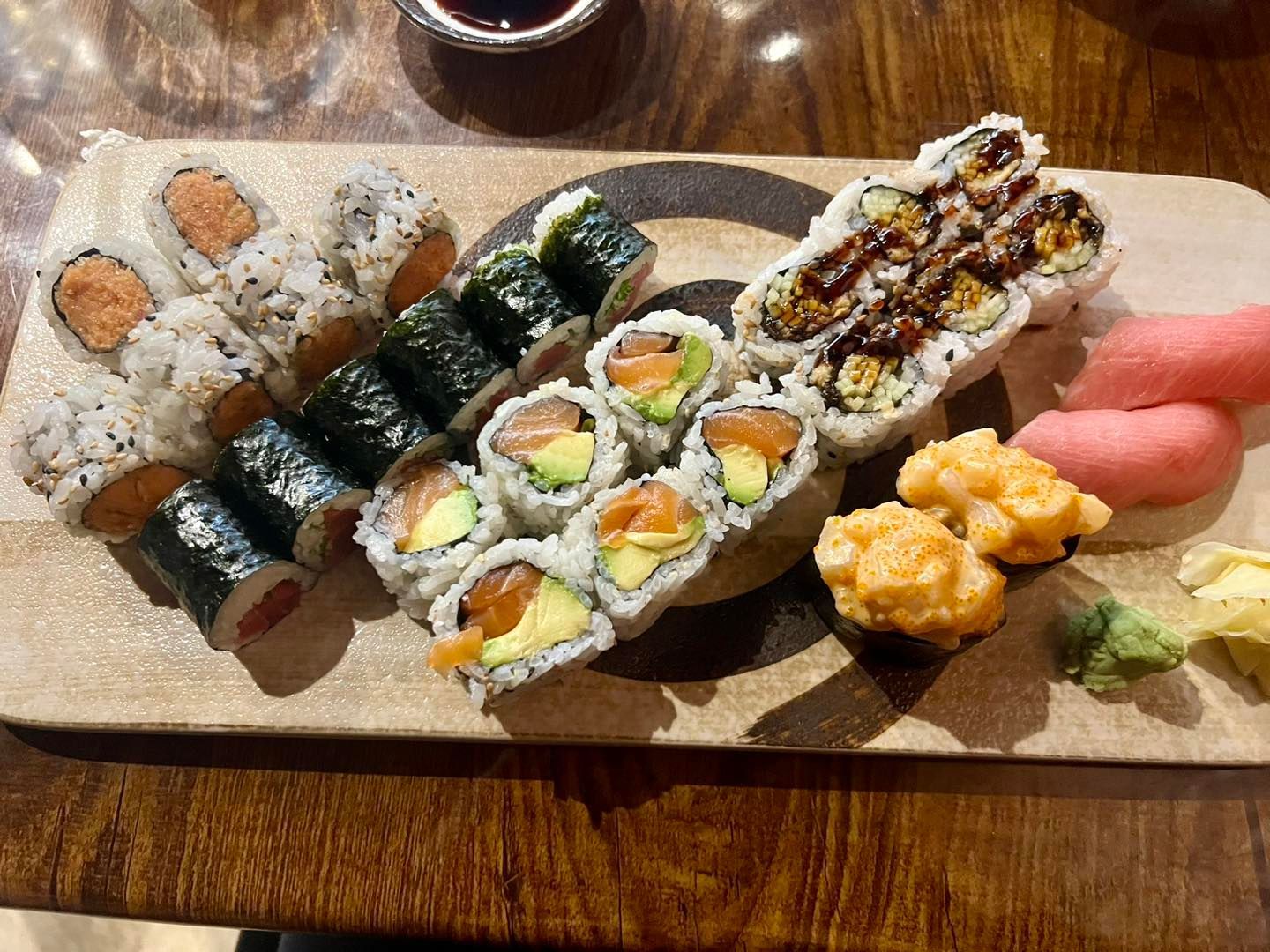 Sushi platter on a wooden board with various rolls and nigiri, including salmon, tuna, and spicy mayo.