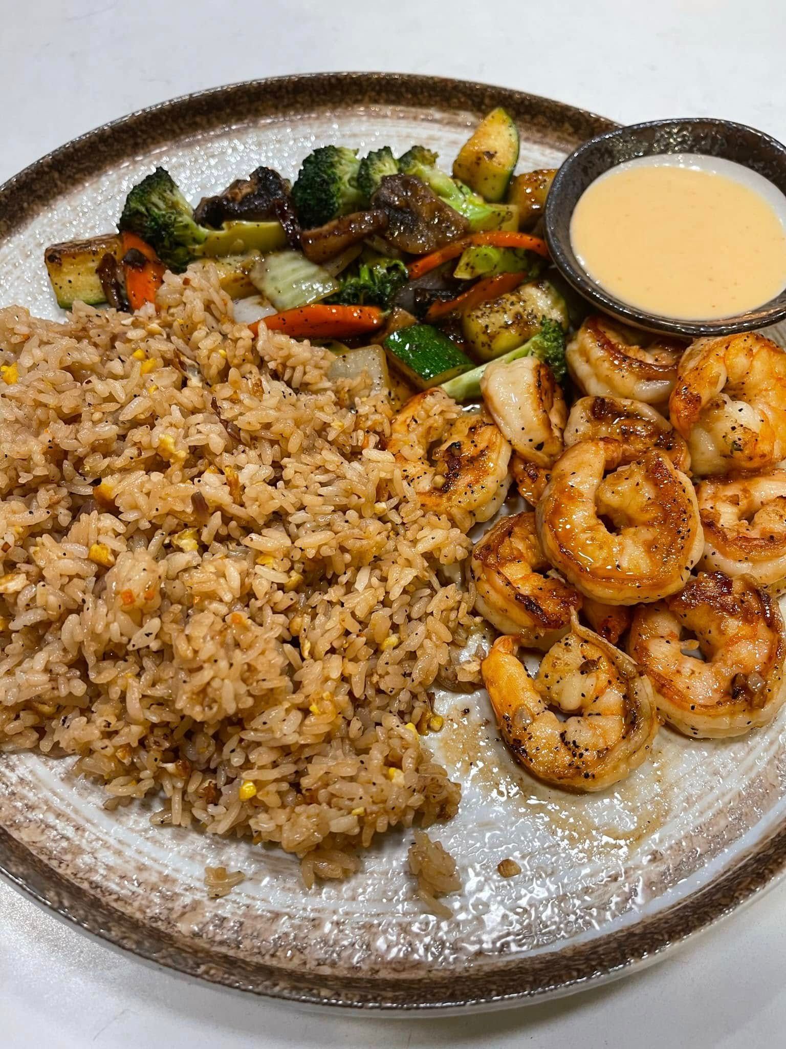 Grilled shrimp, fried rice, vegetables, and dipping sauce on a plate.