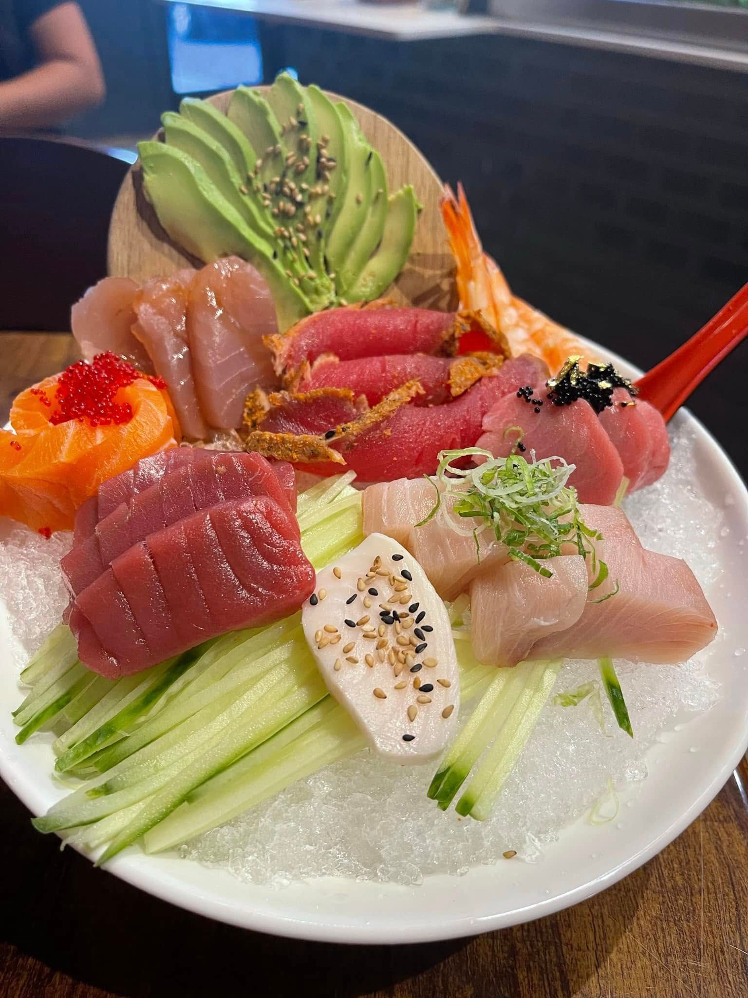 Sushi platter with various sashimi on ice, garnished with avocado, cucumber, and shrimp.