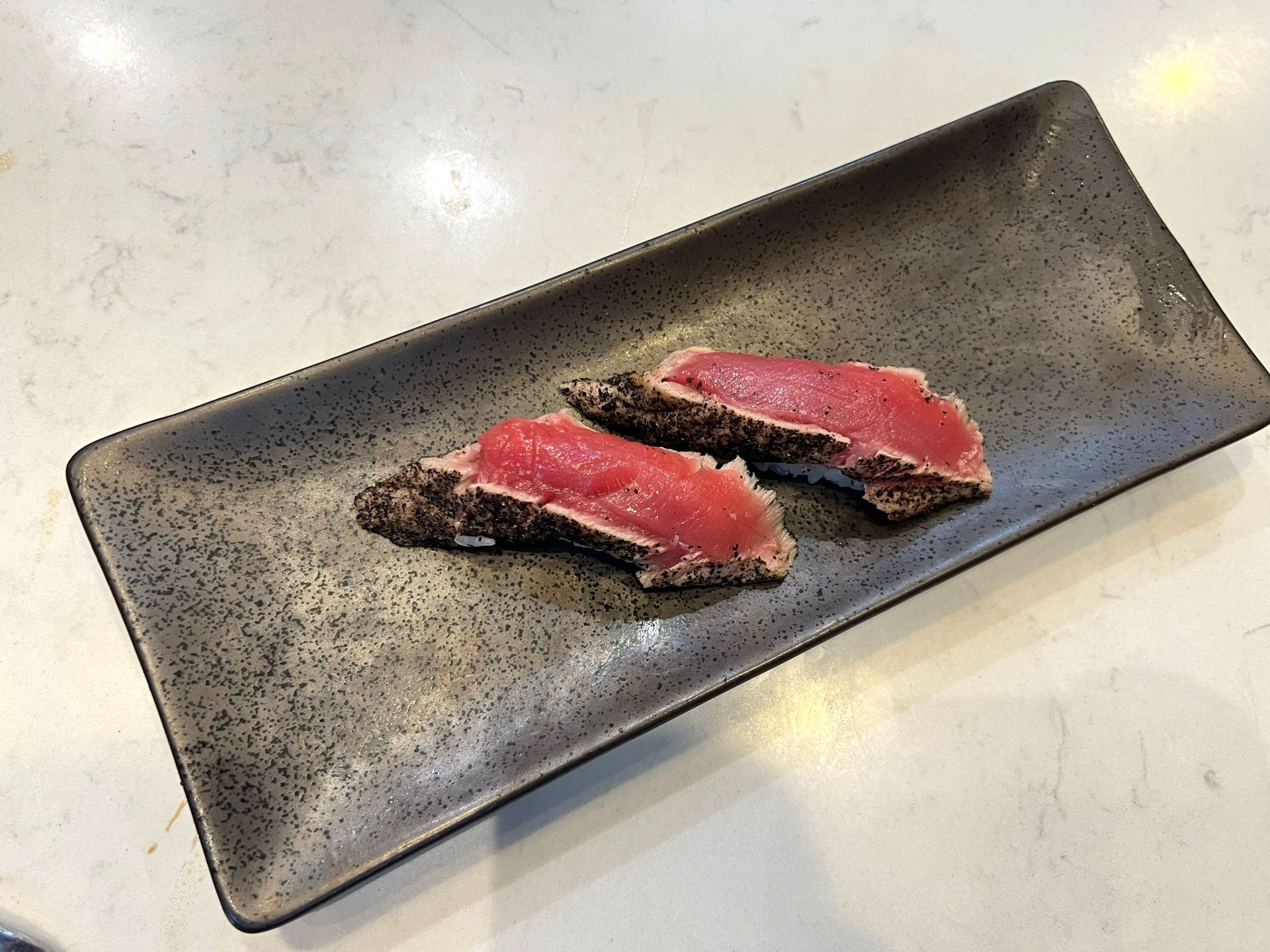 Two seared tuna slices on a dark, rectangular plate.