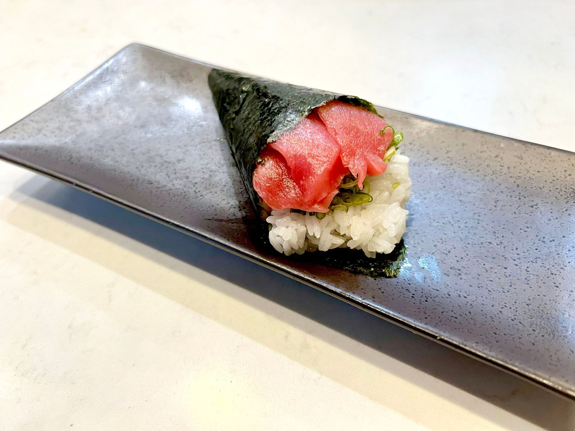 Sushi hand roll, cone-shaped, filled with tuna and rice on a gray rectangular plate.