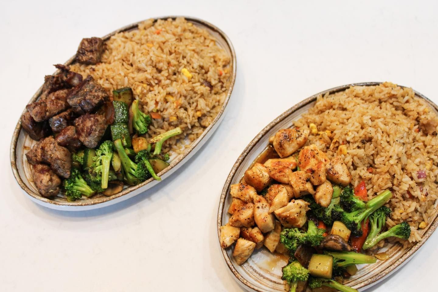 Two plates of food: steak and chicken with fried rice and vegetables.