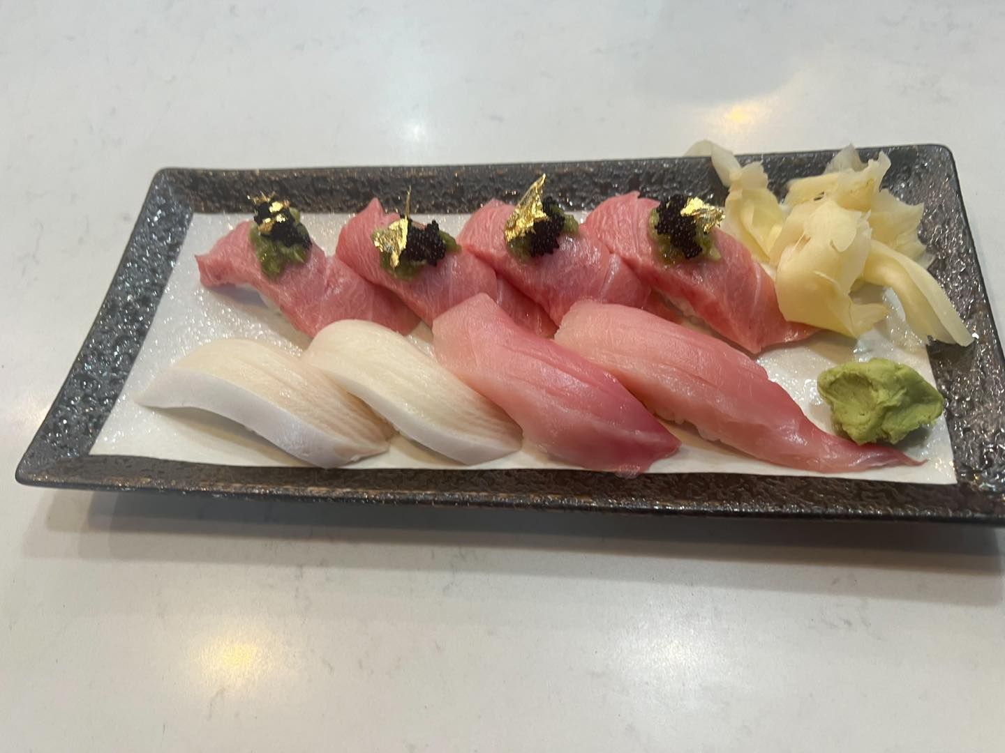 Sushi platter: pink and white fish nigiri, gold flakes, ginger, wasabi.