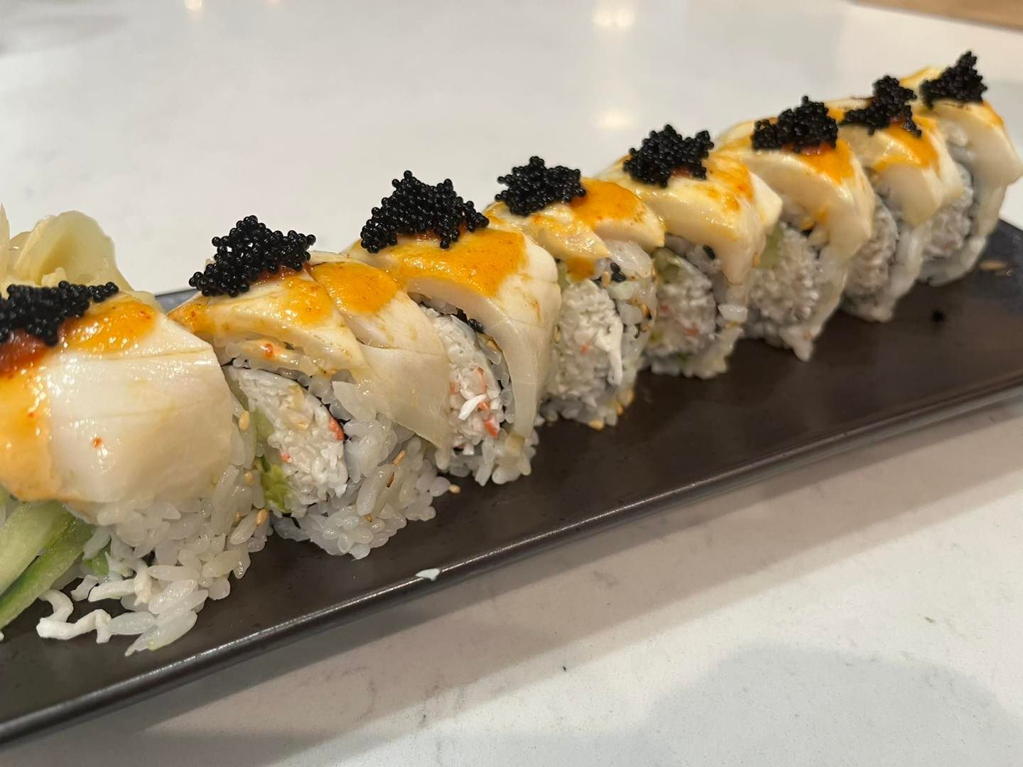Sushi roll with white rice, crab, and fish roe topping on a black rectangular plate.