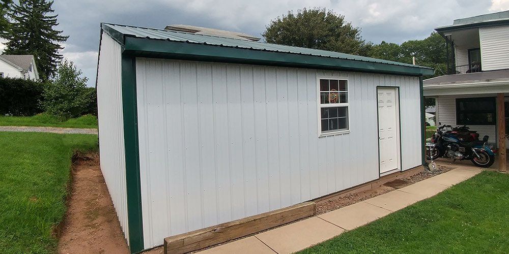 A white shed with a green trim is in the backyard of a house.