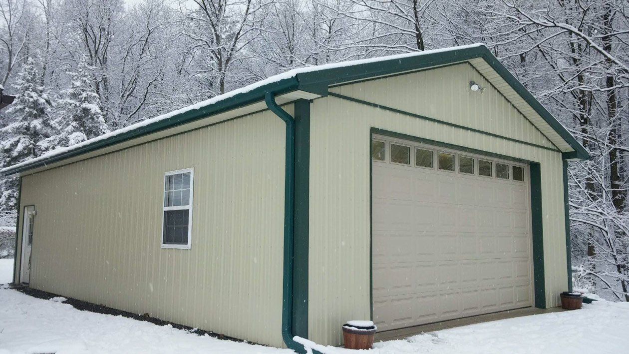 A white garage with a green trim is covered in snow.