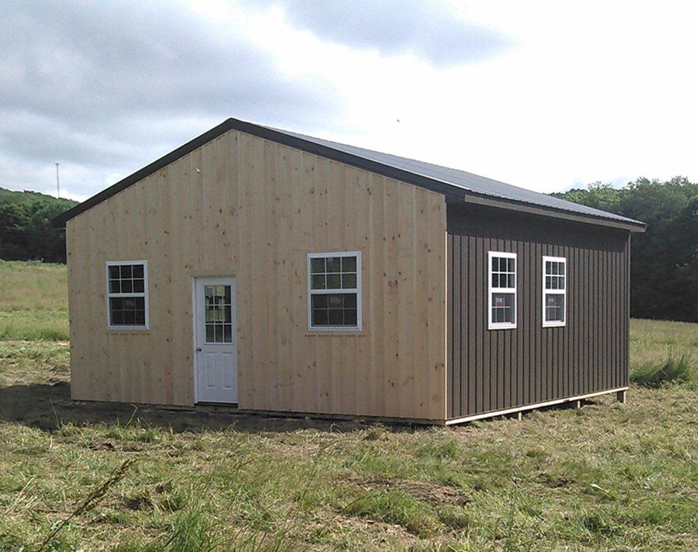A wooden building with a black roof is sitting in the middle of a grassy field.