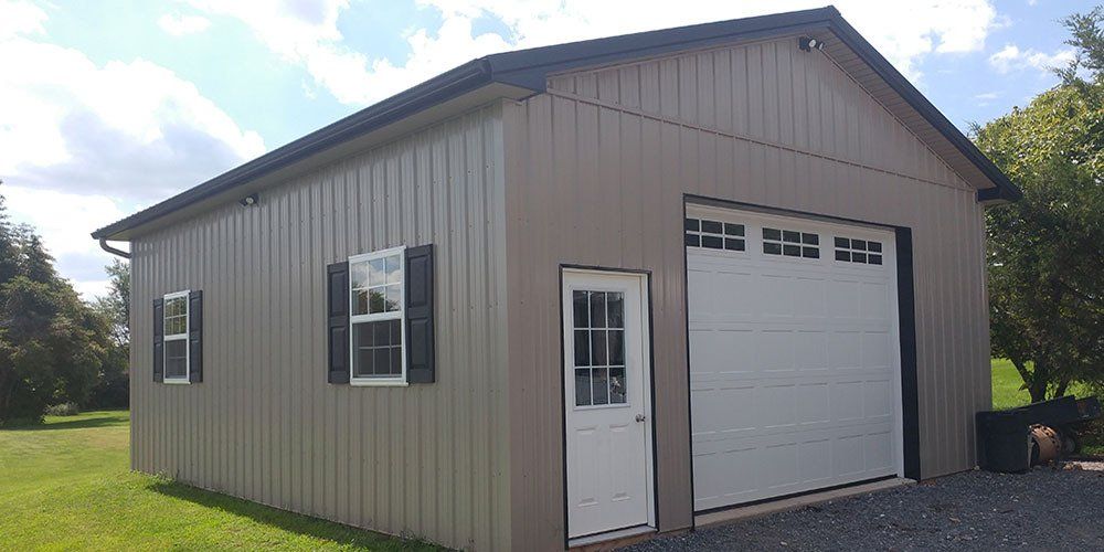 A garage with a white garage door and shutters is sitting in the middle of a grassy field.