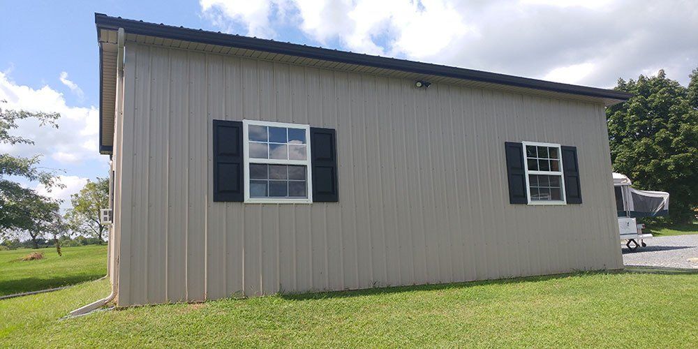 A house with two windows and black shutters is sitting on top of a lush green field.