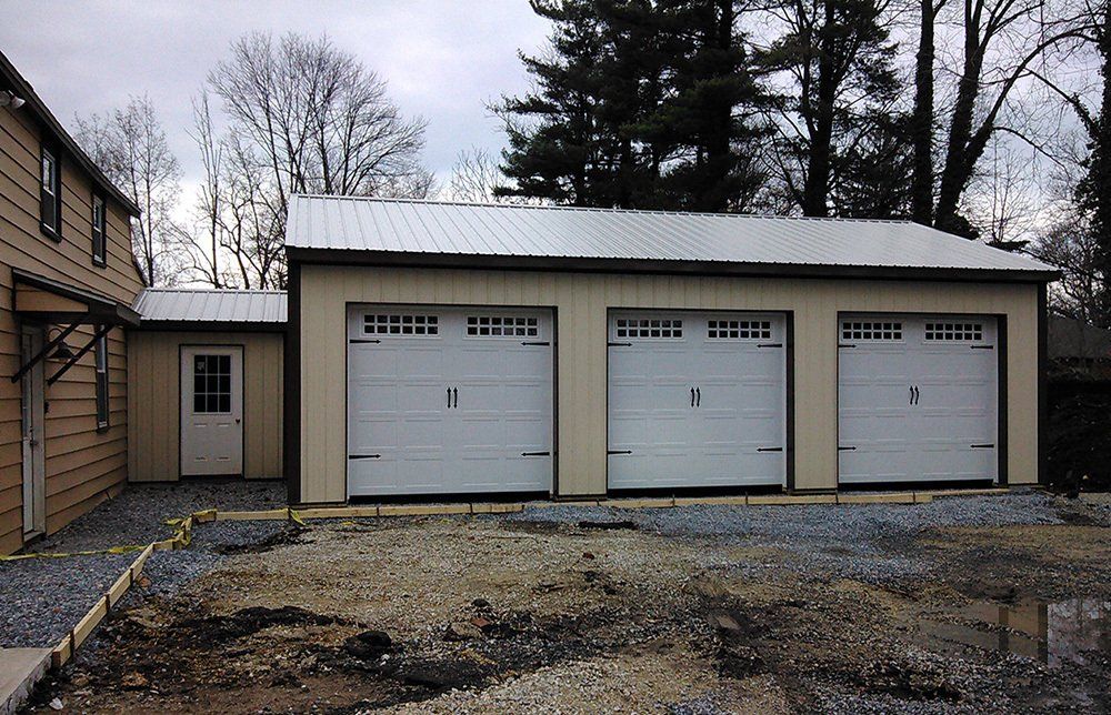 A garage with three white doors and a metal roof