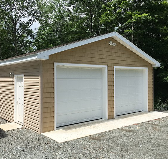 A garage with two white garage doors is surrounded by trees.