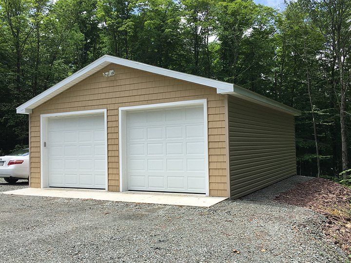 A car is parked in front of a garage with two garage doors.