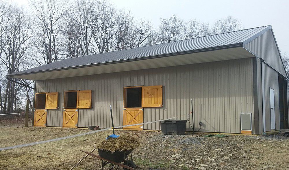 A horse barn with a wheelbarrow full of hay in front of it.