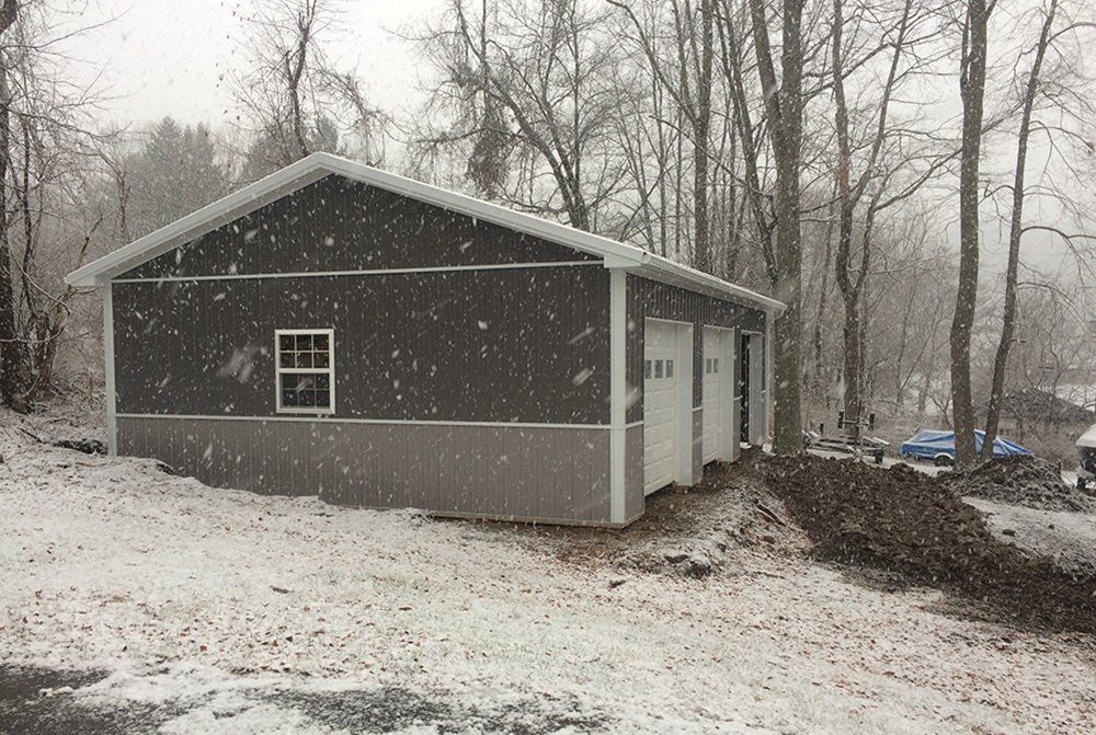A garage with snow falling on it and trees in the background