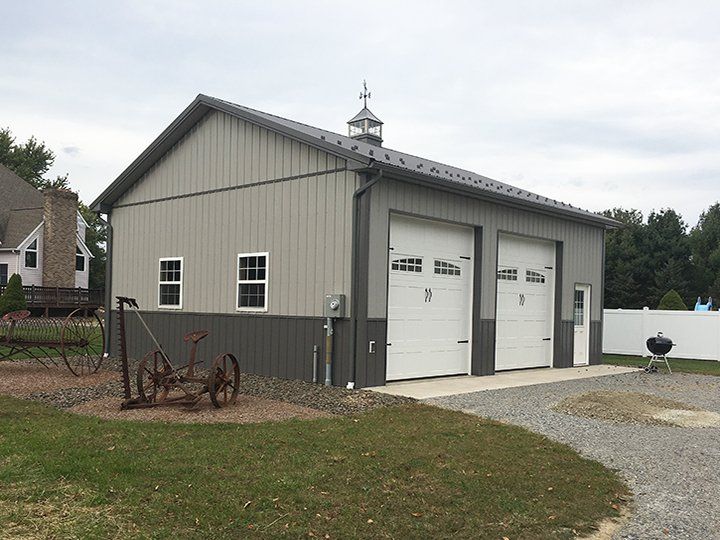 A large garage with three garage doors is sitting in the middle of a grassy field.