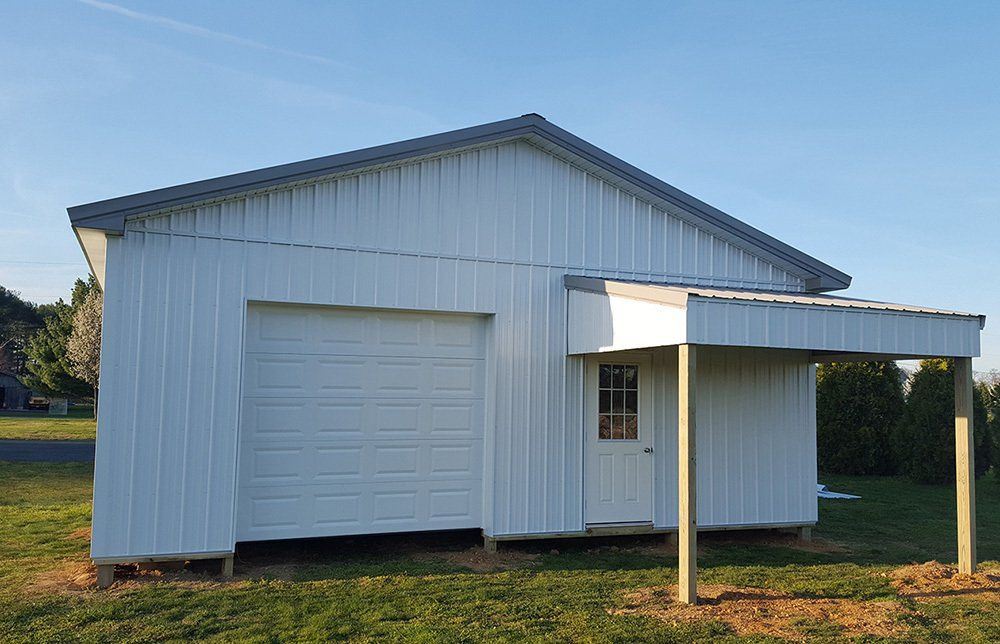 A white garage with a canopy and a door is sitting in the middle of a grassy field.