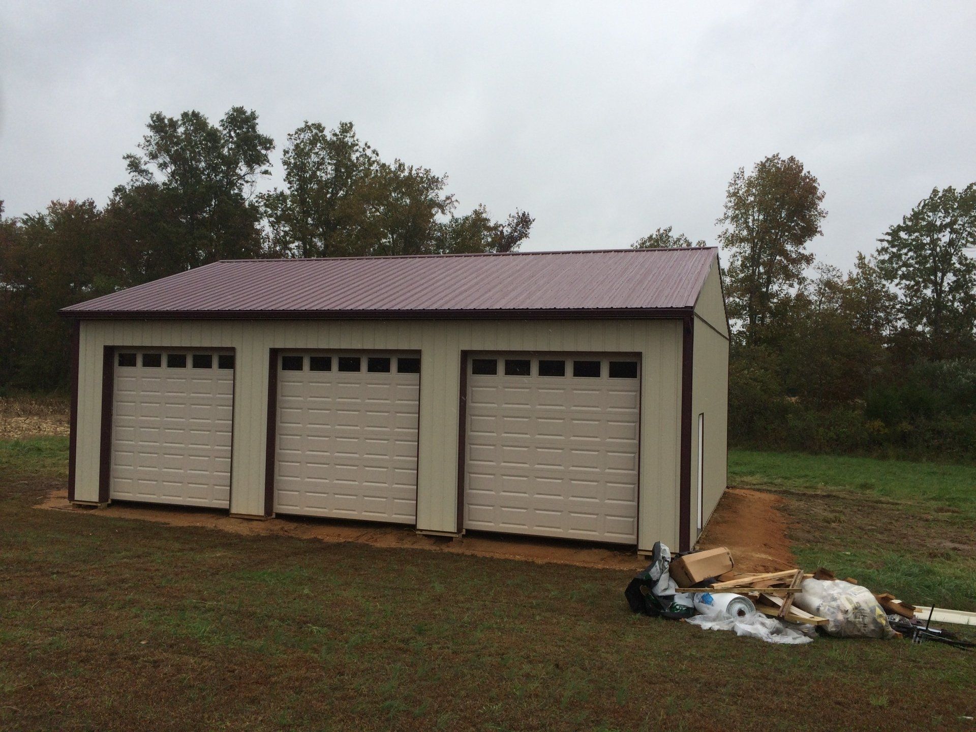 A garage with three garage doors is sitting in the middle of a grassy field.