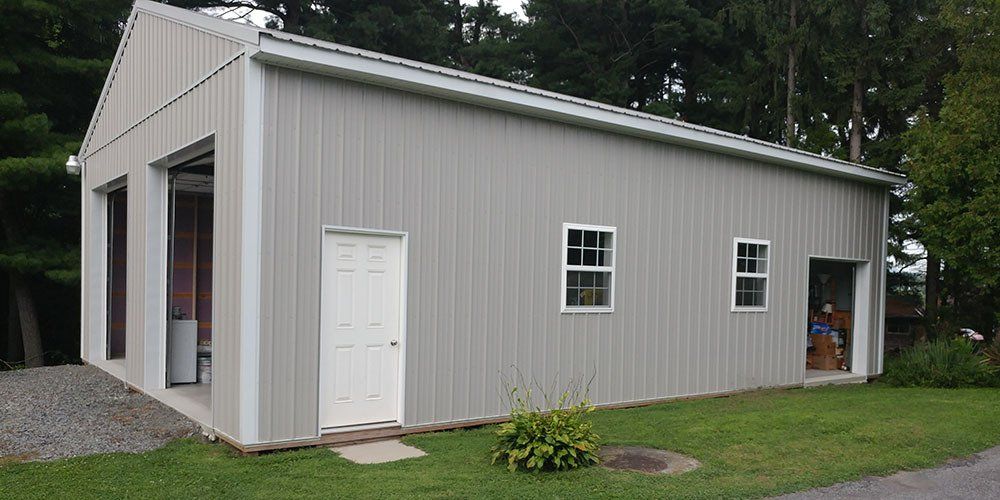 A large gray building with a white door and windows is sitting on top of a lush green field.