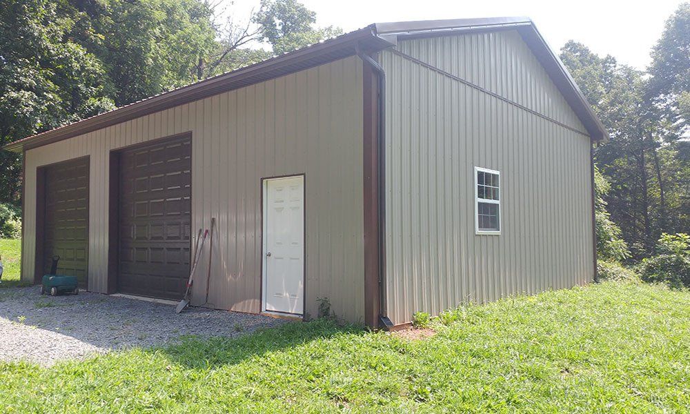 A large metal building with three garage doors and a window is sitting in the middle of a grassy field.