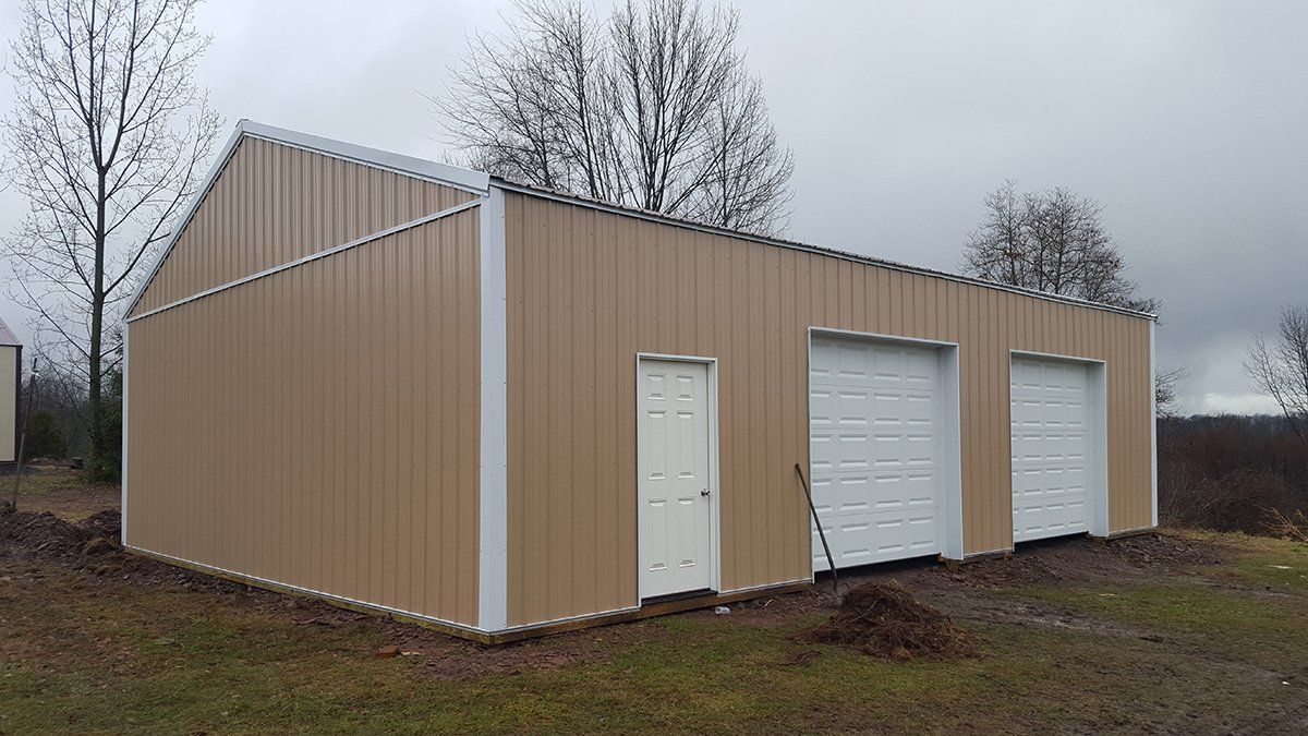 A large metal building with two garage doors is sitting in the middle of a grassy field.
