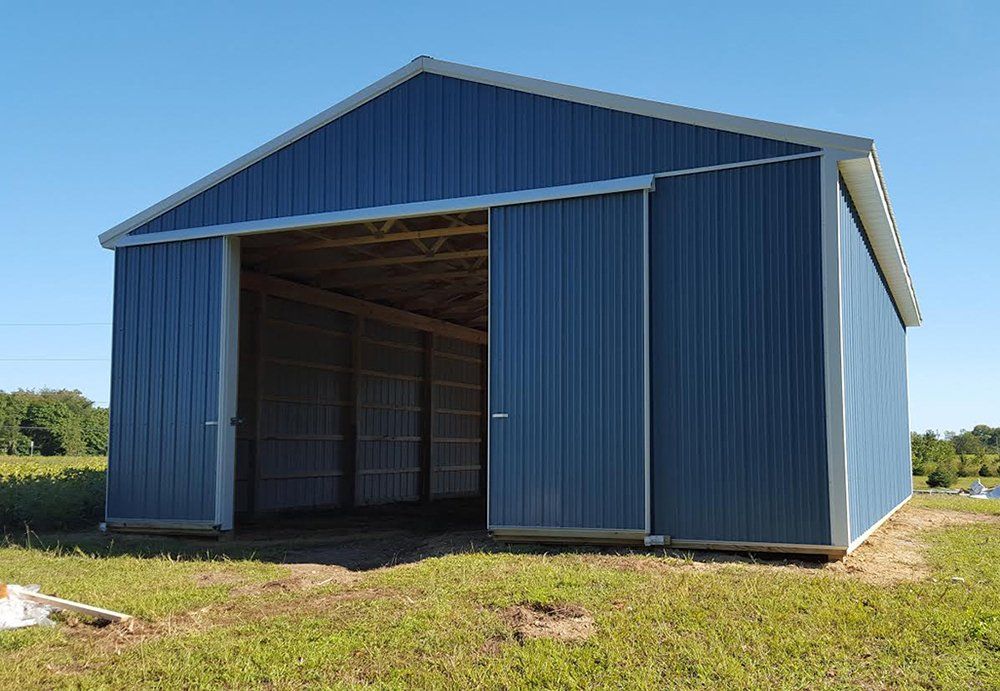 A blue barn with sliding doors is sitting in the middle of a grassy field.
