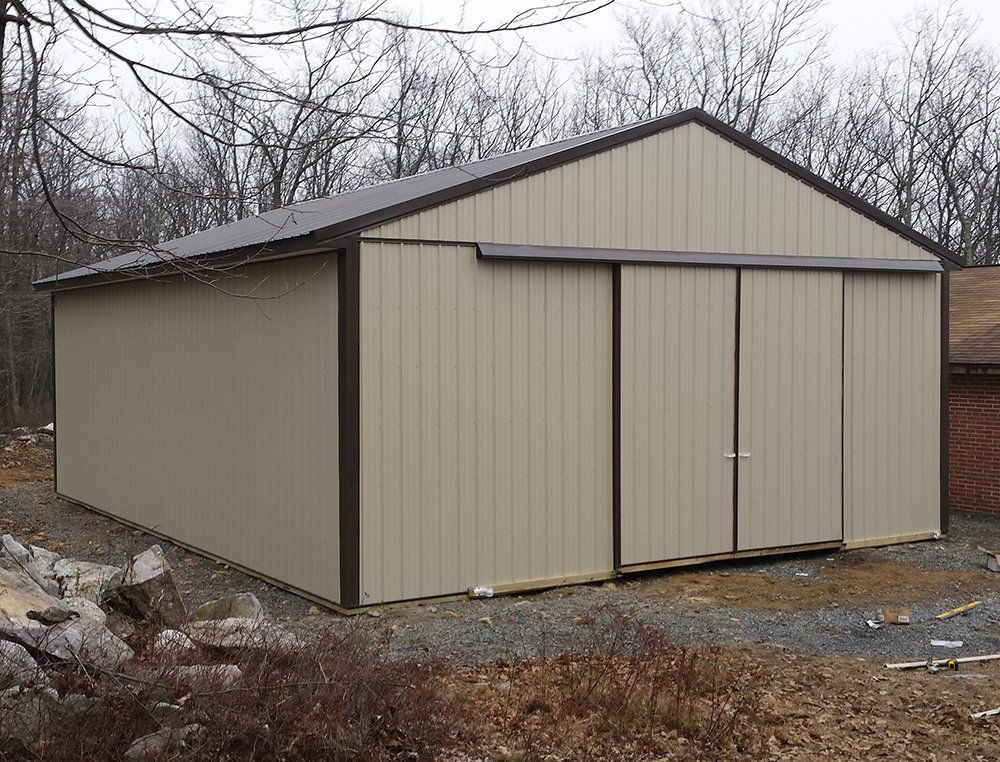 A large metal barn with sliding doors is sitting in the middle of a dirt field.
