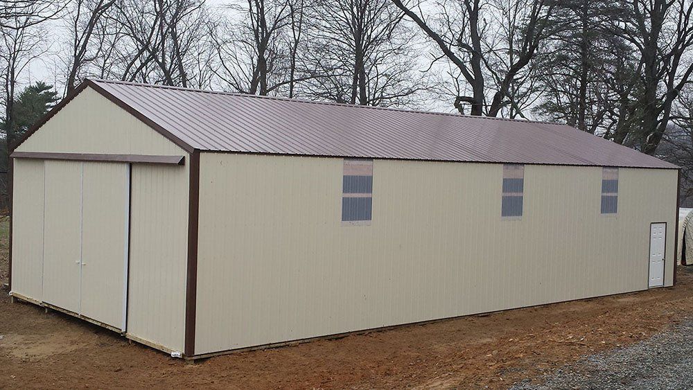 A large white building with a brown roof is sitting on top of a dirt field.
