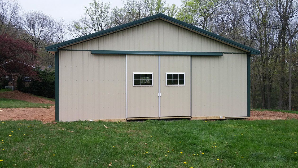 A barn with a sliding barn door is sitting in the middle of a lush green field.