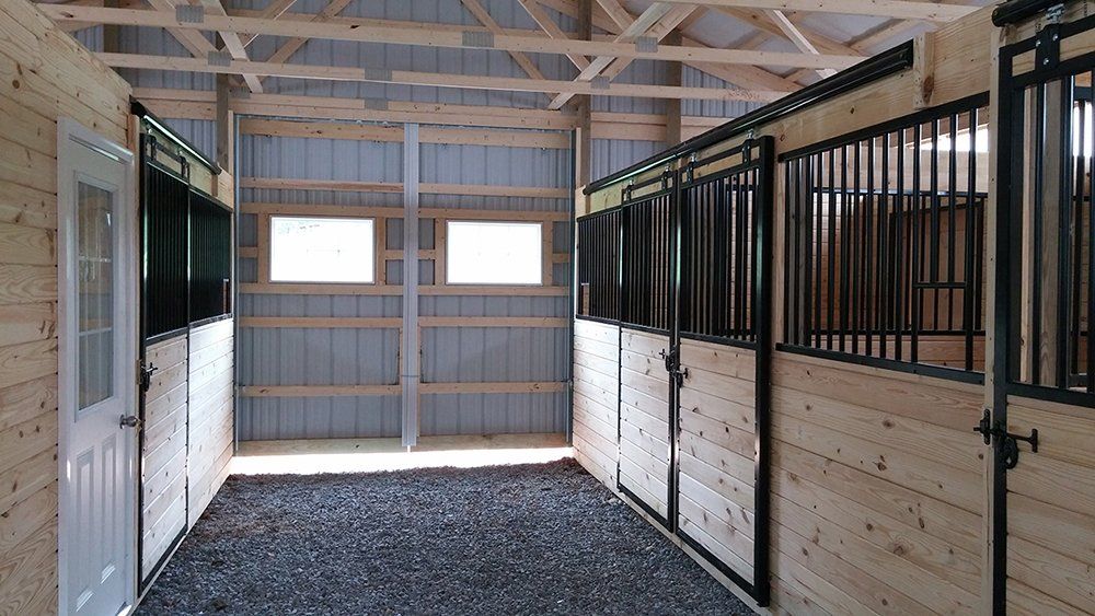 A row of horse stalls in a barn with a gravel floor.