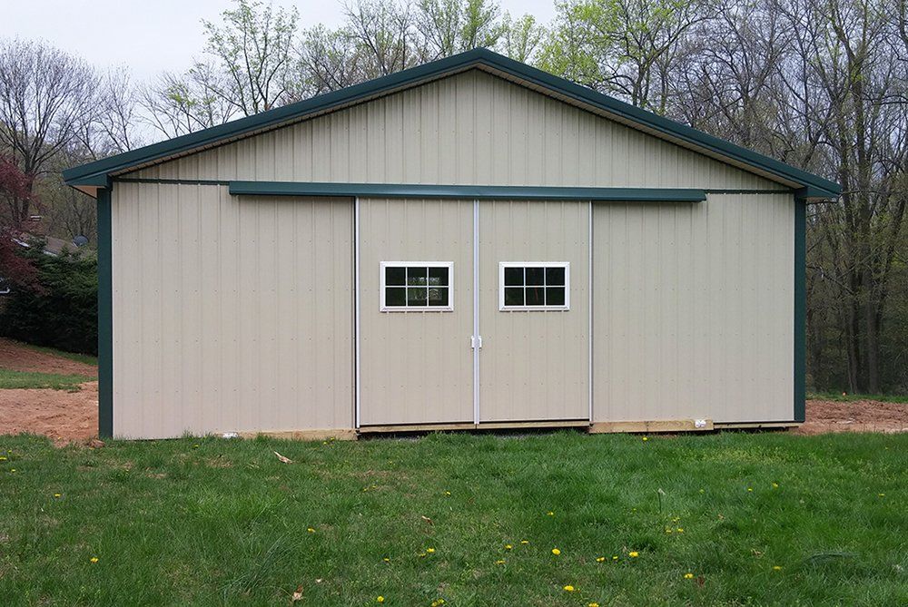 A barn with sliding doors and windows is sitting on top of a lush green field.