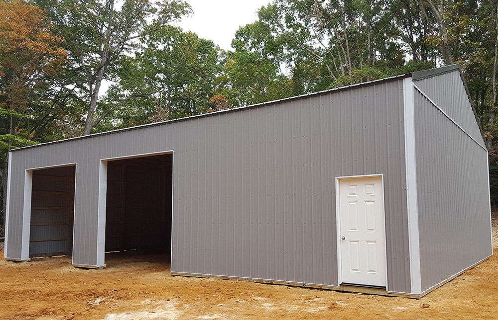 A large gray metal building with a white door is sitting in the middle of a dirt field.