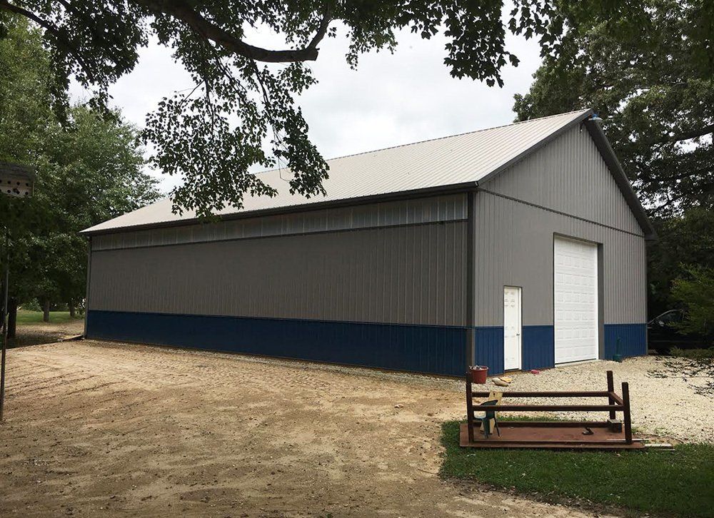A large gray and blue barn with a white door is sitting in the middle of a dirt field.
