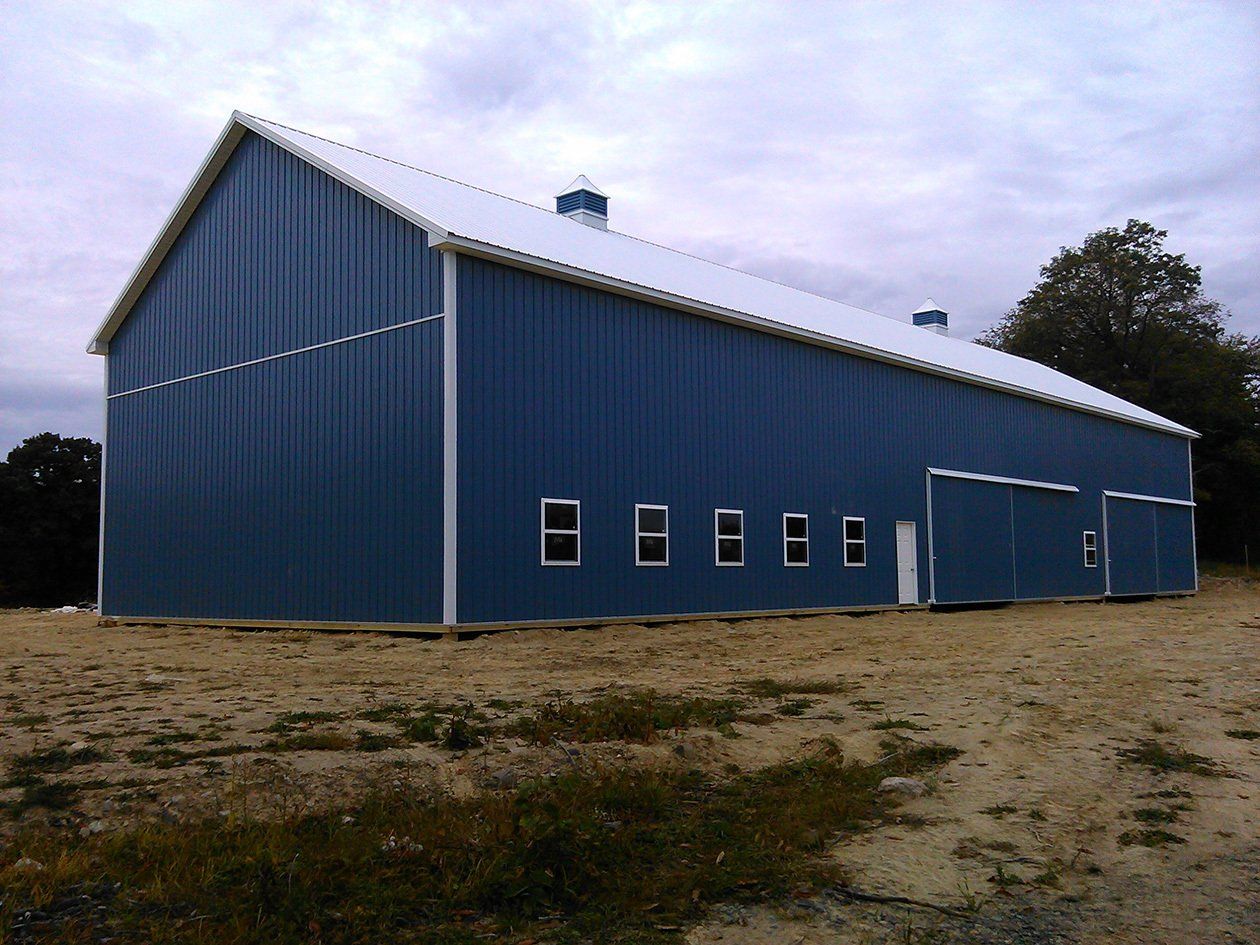 A blue barn with a white roof sits in the middle of a dirt field