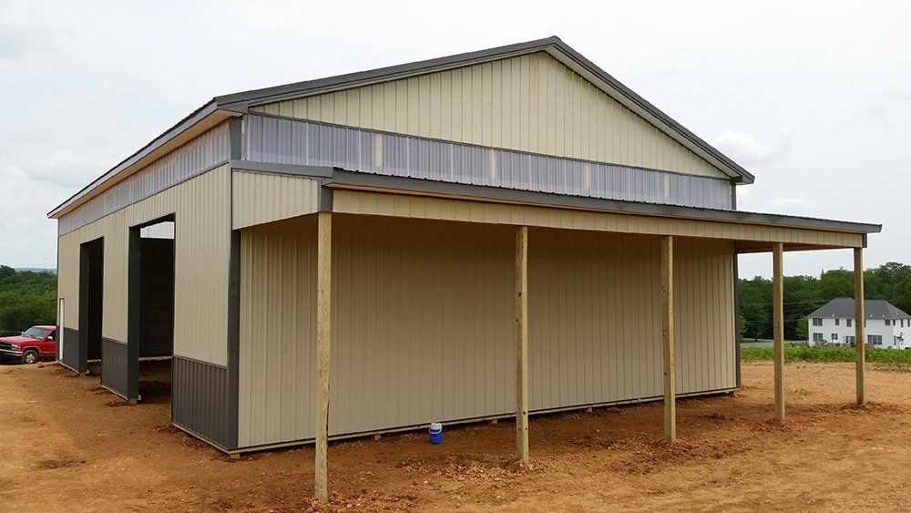 A large metal building with a porch is sitting in the middle of a dirt field.