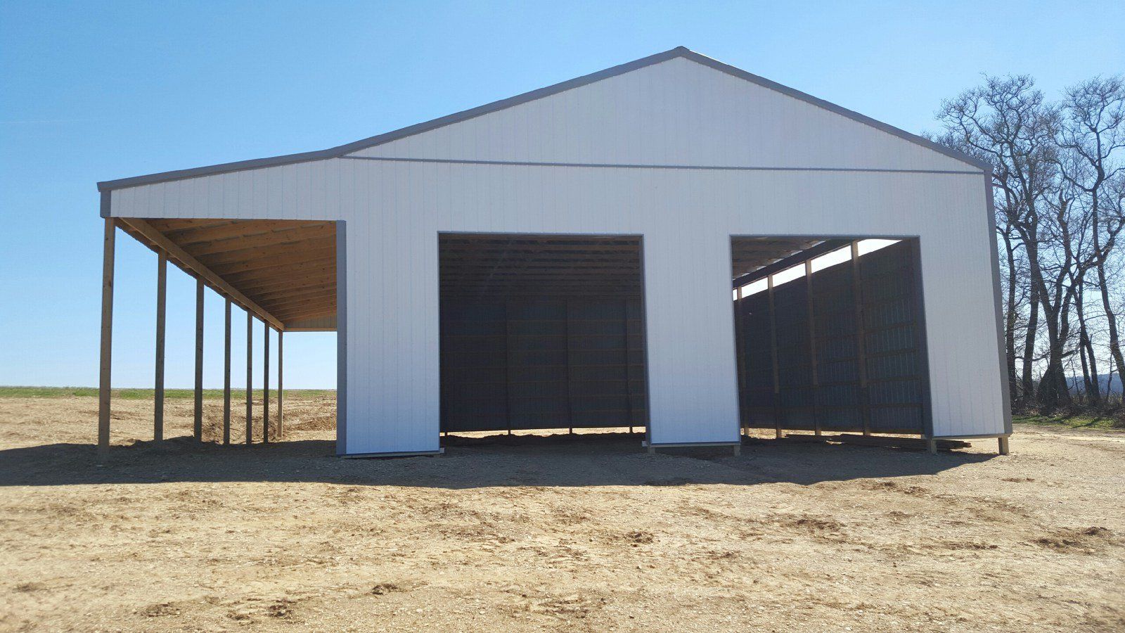 A white building is sitting in the middle of a dirt field.