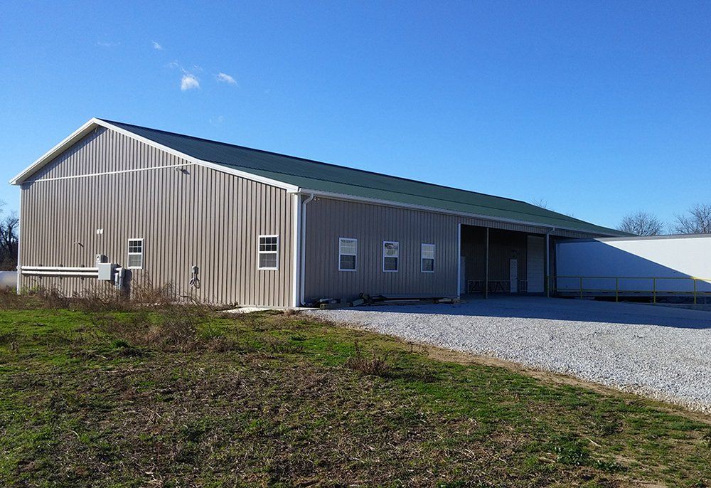 A large metal building with a green roof is sitting in the middle of a grassy field.