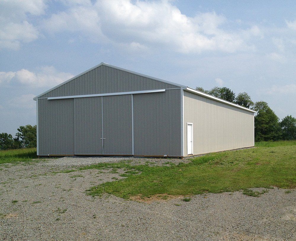 A large gray building with a white door is in the middle of a grassy field