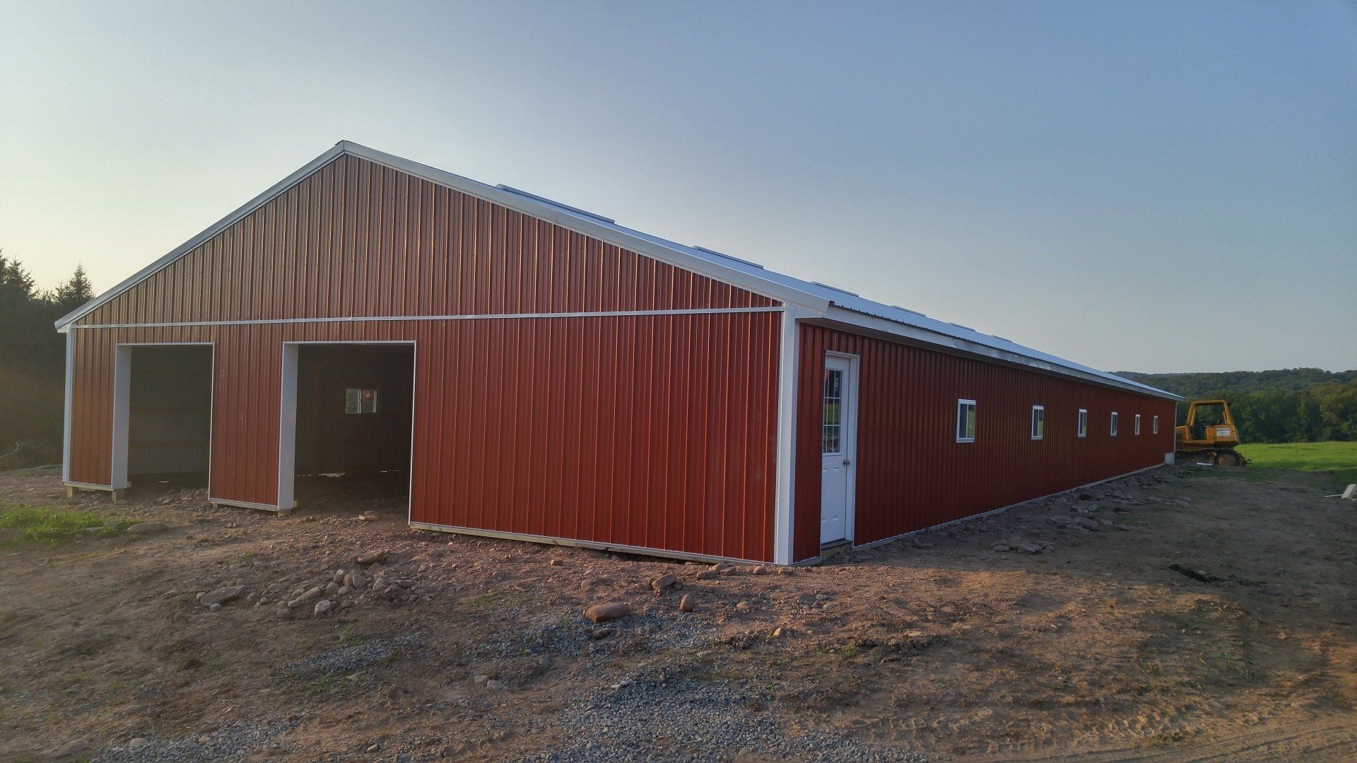 A large red barn is sitting in the middle of a dirt field.