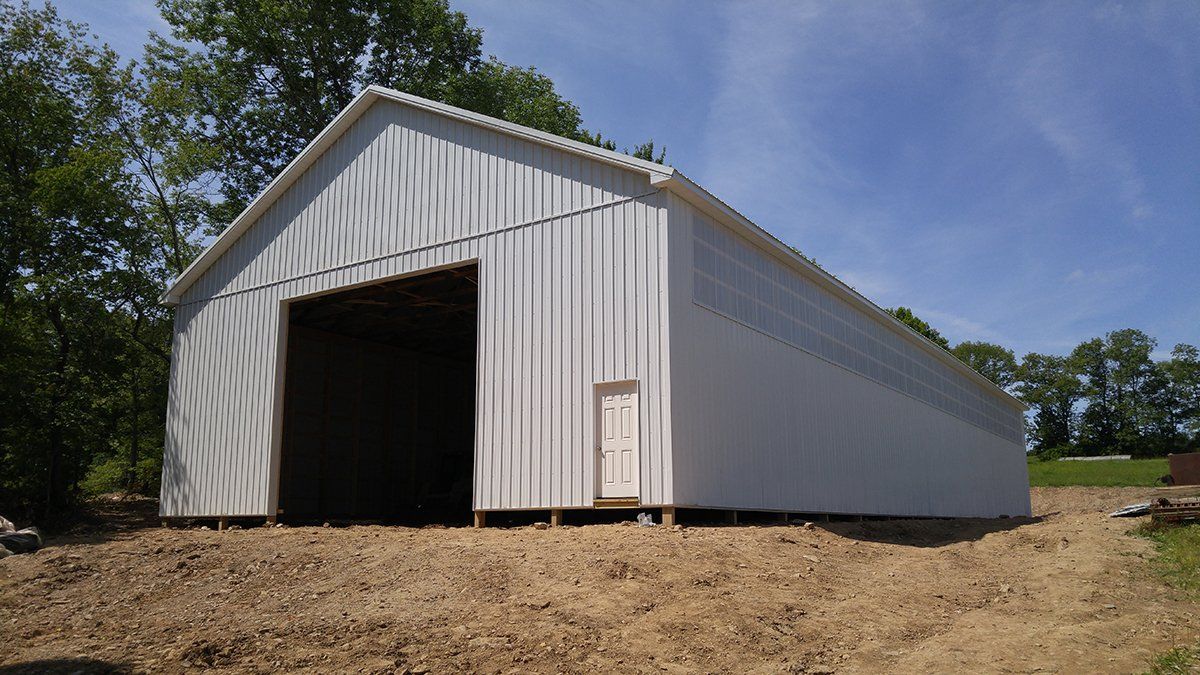 A large white barn is sitting on top of a dirt hill.
