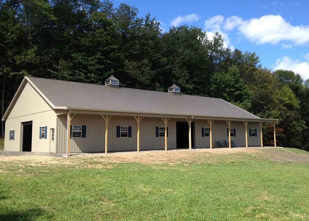 A large building with a porch is sitting in the middle of a grassy field.