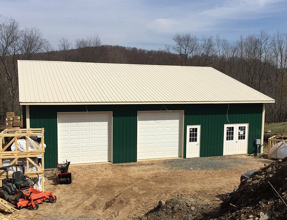 A green barn with white doors and a white roof is being built.