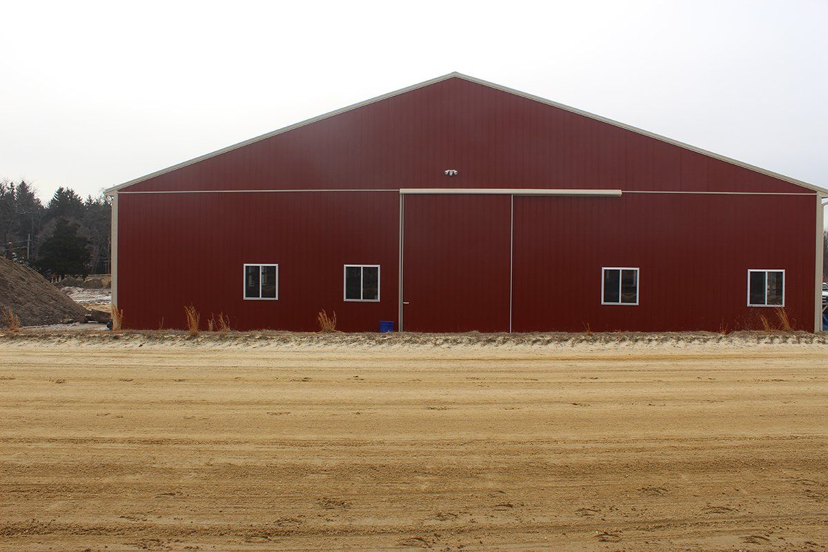 A large red barn is sitting in the middle of a dirt field.