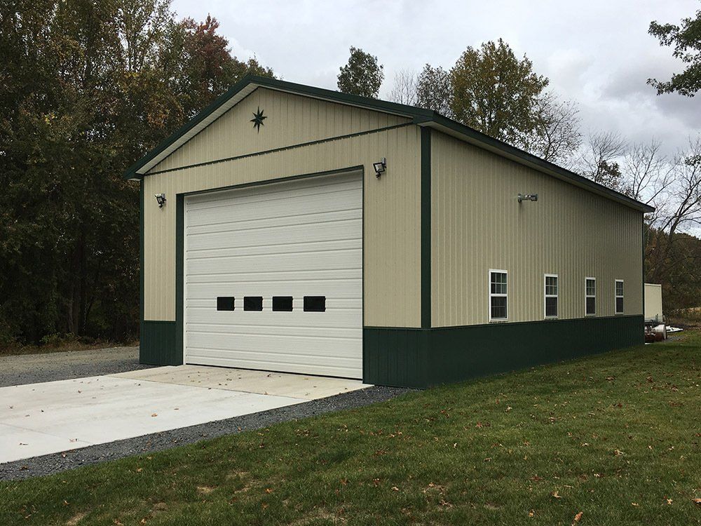 A large garage with a large white garage door is sitting in the middle of a grassy field.
