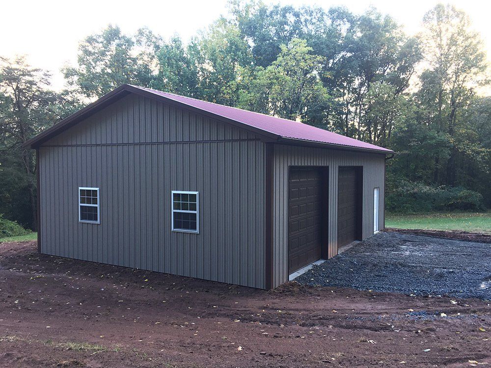 A garage with a red roof is sitting in the middle of a dirt field.