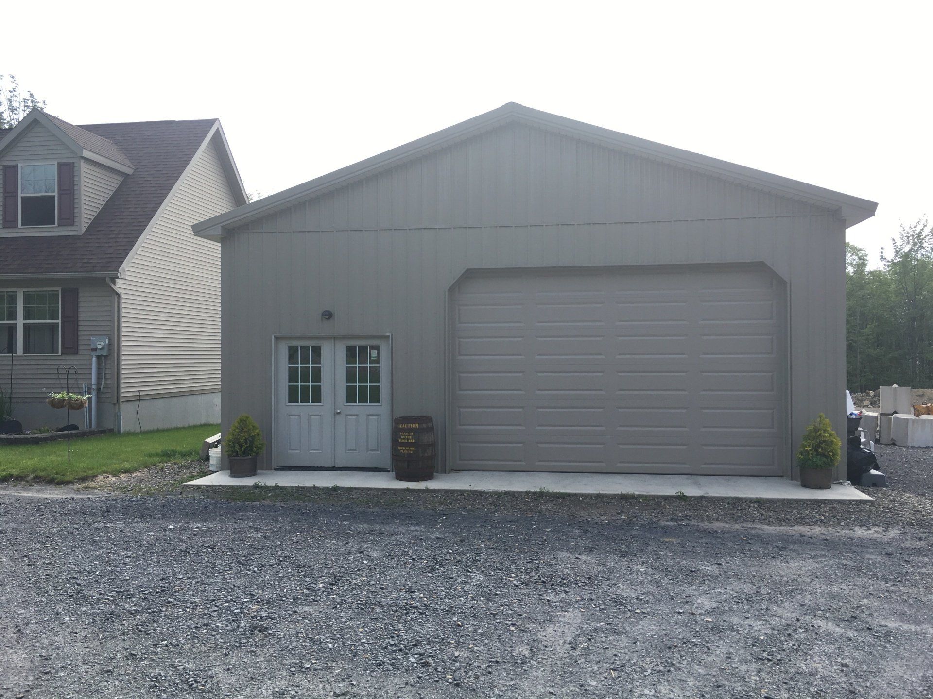 A garage with a barrel in front of it and a house in the background.