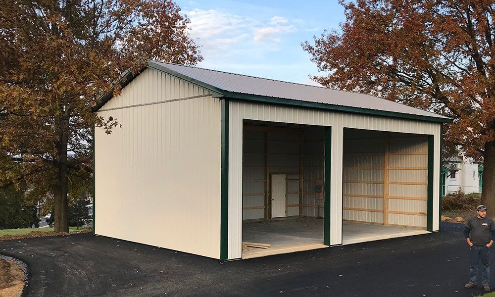 A white garage with a green trim is sitting on top of a dirt road.