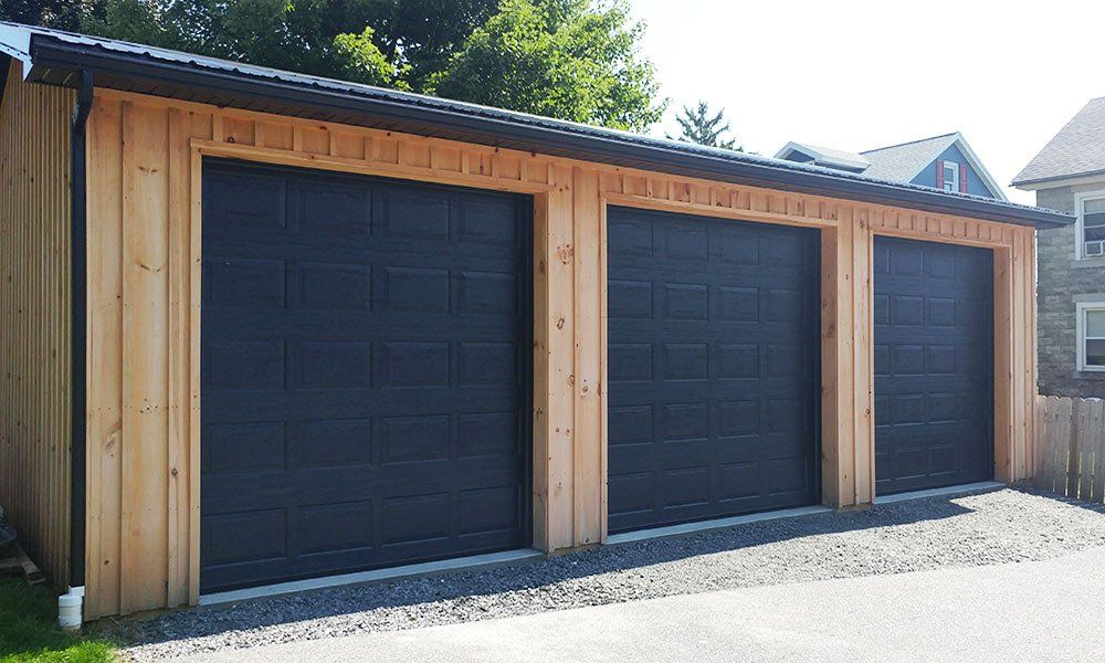 A garage with three black garage doors is sitting next to a house.